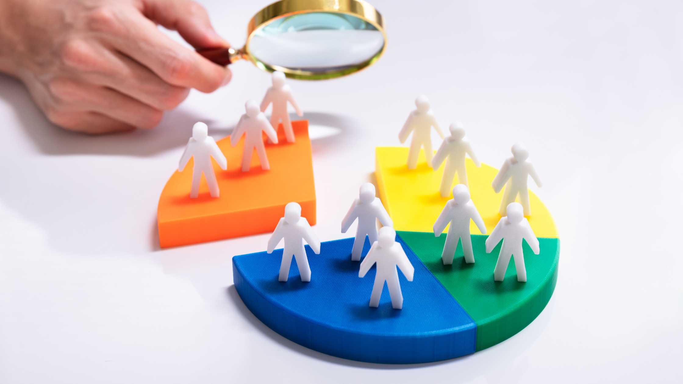 A magnifying glass inspecting small, white figurines placed on different colored pie-chart segments, representing audience or email segmentation.