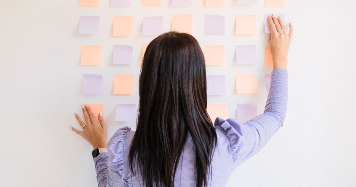 A woman organizing pastel-colored sticky notes on a wall, symbolizing structured planning for an email marketing strategy.