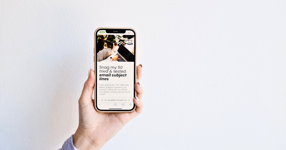 Hand holding a smartphone displaying a guide titled ‘Snag my 50 tried & tested email subject lines,’ promoting a free resource for email marketing tips.”